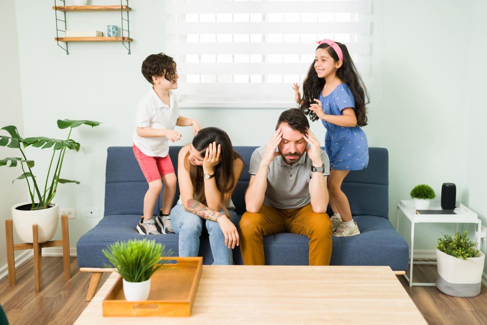 stressed-upset-young-parents-feeling-tired-while-their-misbehaved-children-and-jump-on-the-couch-around-them (1)